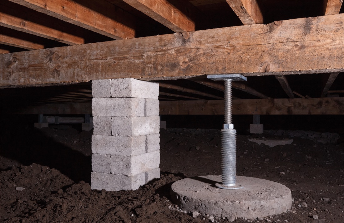 A concrete block pier and an adjustable steel support post carrying a wooden girder inside a crawl space